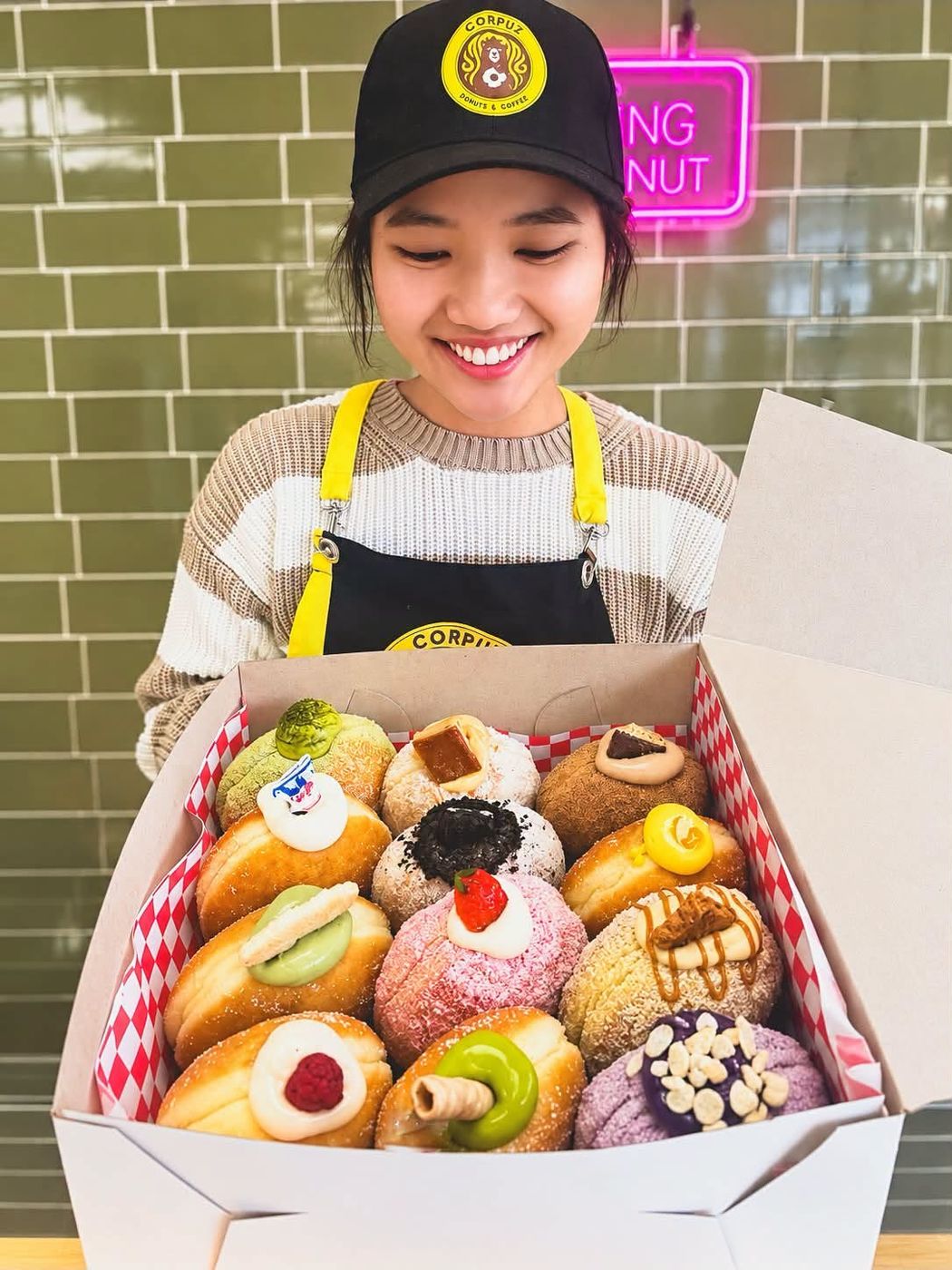 A baker holding a full box of assorted donuts